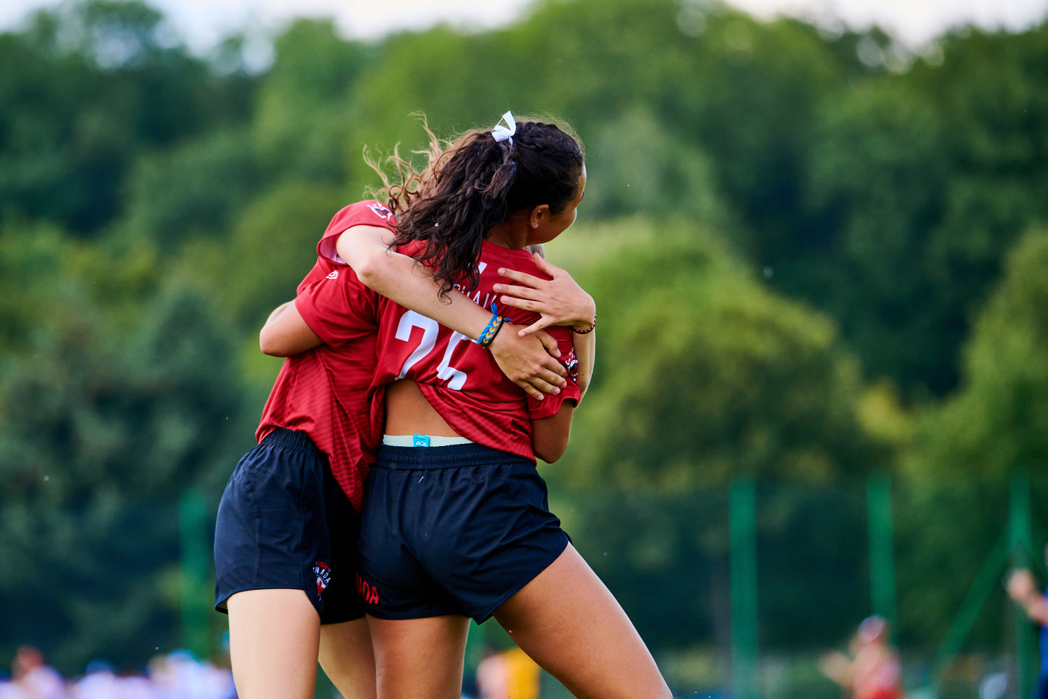 Two JJUC 2022 Ultimate Frisbee athletes hugging each other in their Official Team Canada uniforms, made by VC Ultimate